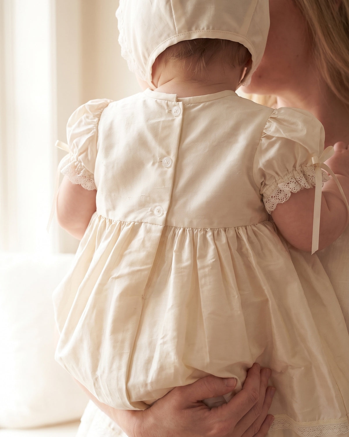 Back view of baby girl white ivory silk christening gown held by mother — Josephine Gown Set by Bonbon Rue
