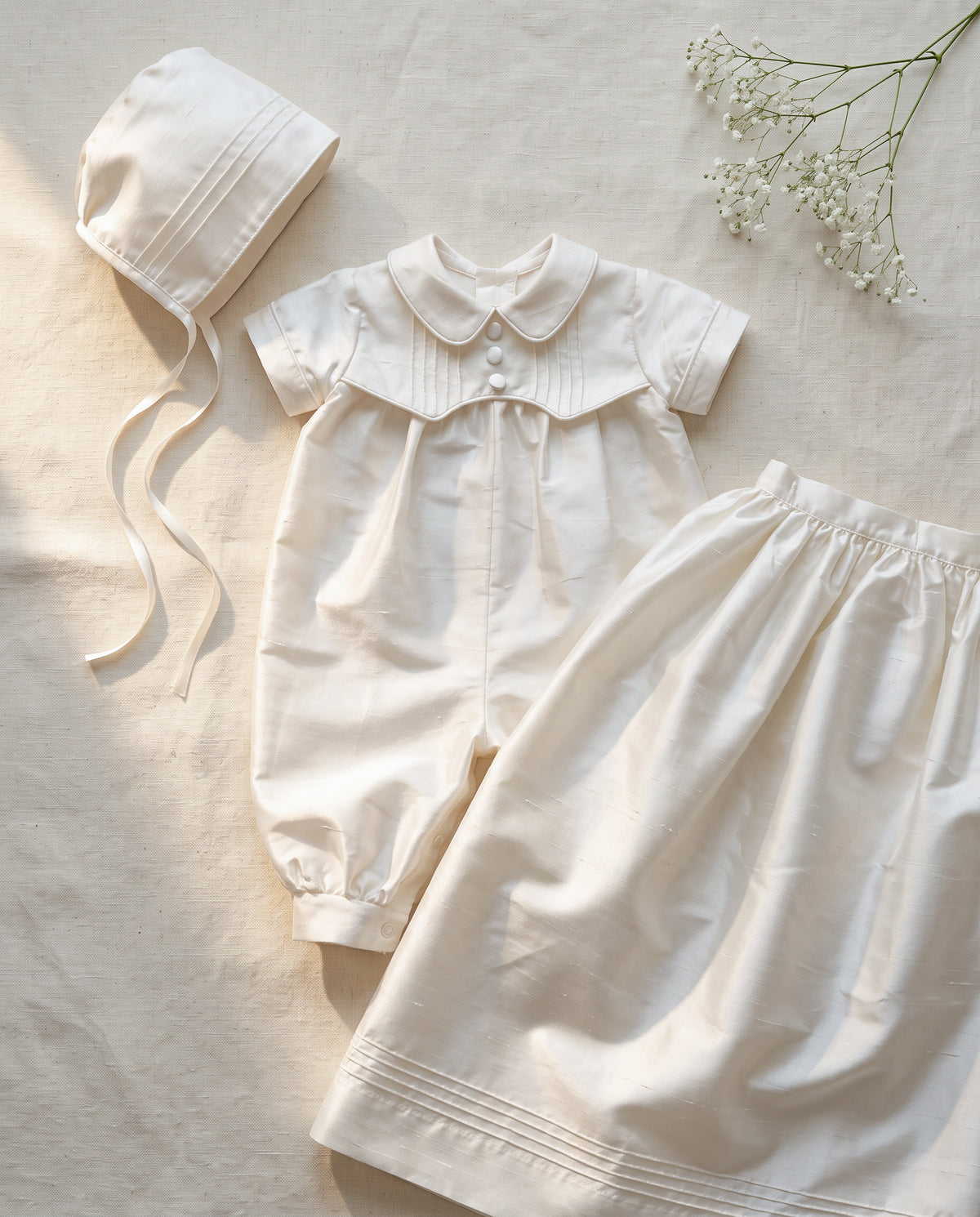 Styled flat lay of white ivory silk baptism gown — Arland Convertible Set in Silk by Bonbon Rue
