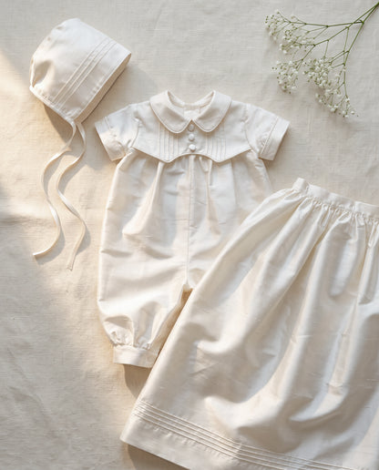 Styled flat lay of white ivory silk baptism gown — Arland Convertible Set in Silk by Bonbon Rue